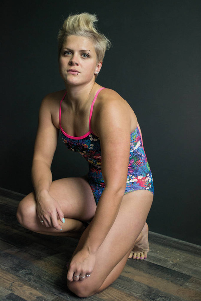 Fotografia sportowa dziewczyna siedzi w strój kąpielowy szary tło - Zdjęcie, obraz