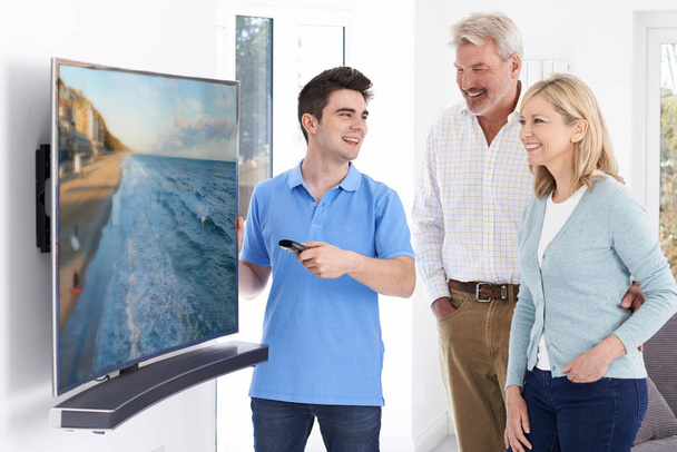 homem demonstrando novo televisão para maduro casal no casa
 - Foto, Imagem