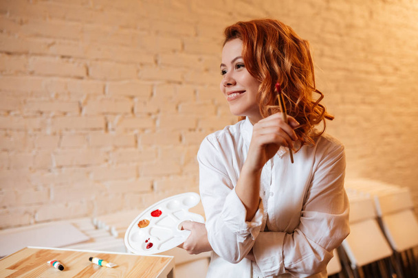Cheerful redhead woman painter with oil paints and palette - Photo, Image