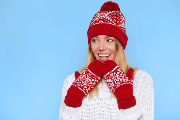 Surprised happy beautiful woman looking sideways in excitement. Christmas girl wearing knitted warm hat and mittens, isolated on blue background - Foto, immagini