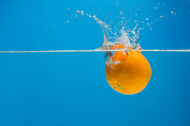 Tangerine in water with splashes on a blue background - Foto, immagini