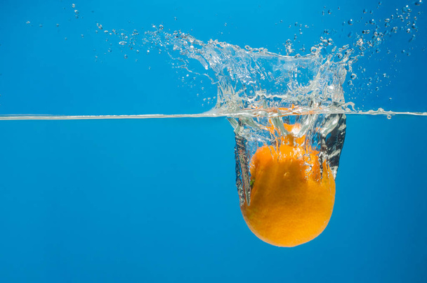 Tangerine in water with splashes on a blue background - Photo, Image