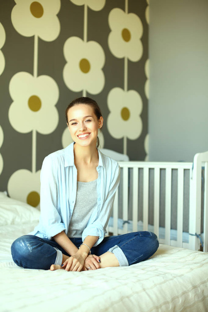 Young woman sitting on the bed near childrens cot - Foto, afbeelding