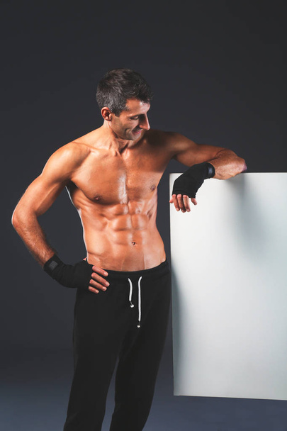 Strong athletic man standing near board on black background - Zdjęcie, obraz