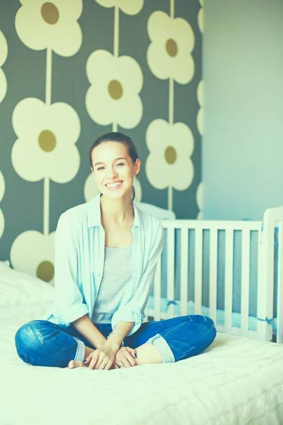 Young woman sitting on the bed near childrens cot - Foto, imagen