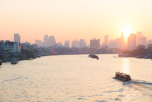 Sonnenaufgang über der malerischen Skyline von Bangkok, Thailand, im Gegenlicht bei Sonnenaufgang mit orangerotem, klarem Himmel. Boote auf dem chao phraya Fluss. - Foto, Bild