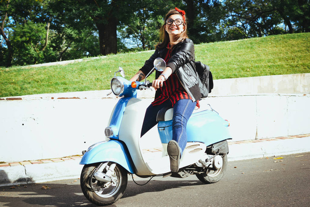 Happy young hipster woman in glasses driving a vintage scooter in city - Foto, Imagem