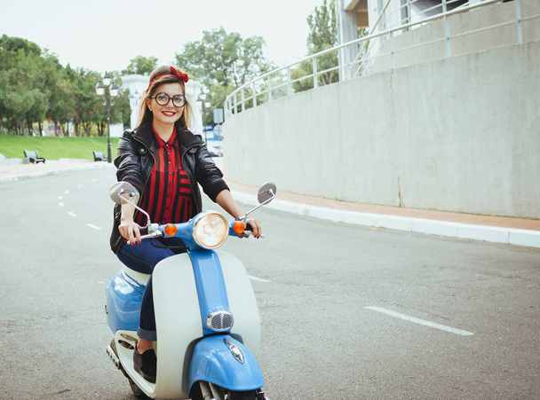 Happy young hipster woman in glasses driving a vintage scooter in city - Foto, immagini