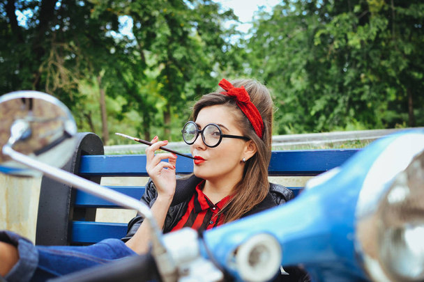 Young hipster woman in glasses sitting on a bench and smoking cigarette - Zdjęcie, obraz