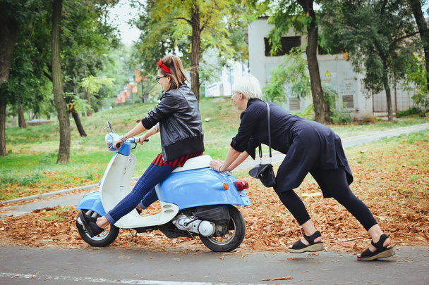 Two young women having some fun with vintage scooter in park - Fotografie, Obrázek