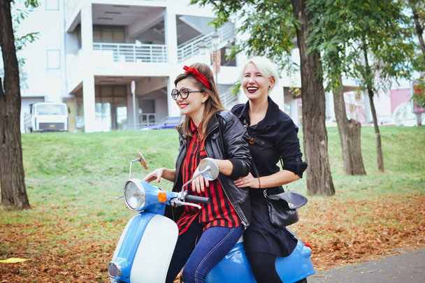 Two young women having some fun with vintage scooter in park - Фото, зображення