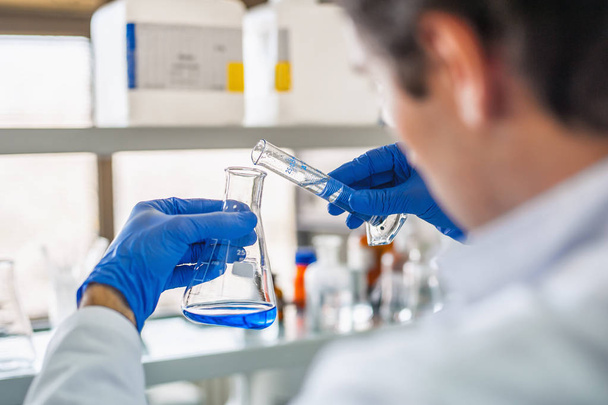 Αρσενικό εργαστήριο ερευνητής εκτελεί δοκιμές με μπλε υγρό - Φωτογραφία, εικόνα