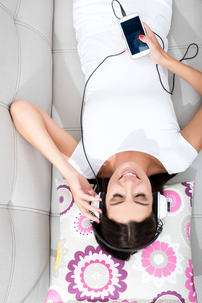 Beautiful young woman laying on the couch listening to music  - Fotoğraf, Görsel