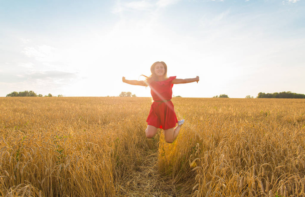 Beauty Girl Outdoors enjoying nature. Beautiful Teenage Model girl in red dress jumping on summer or autumn Field.. Free Happy Woman. - Фото, изображение