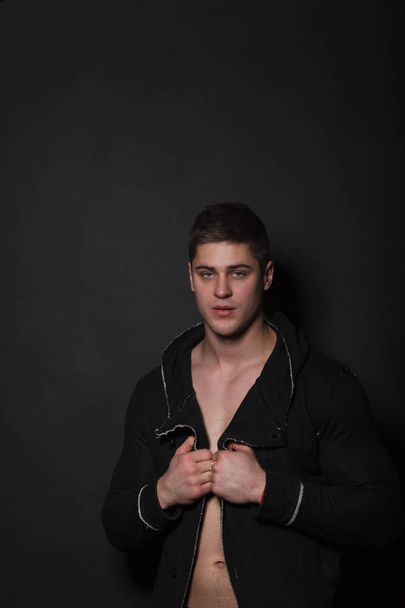 Fashionable man standing on a black background. Muscular man in black sweater - Foto, immagini