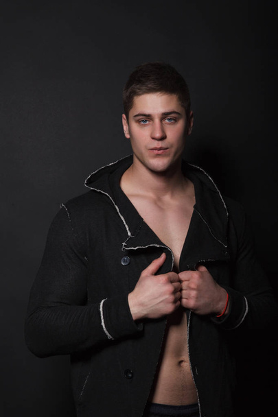 Fashionable man standing on a black background. Muscular man in black sweater - Photo, Image