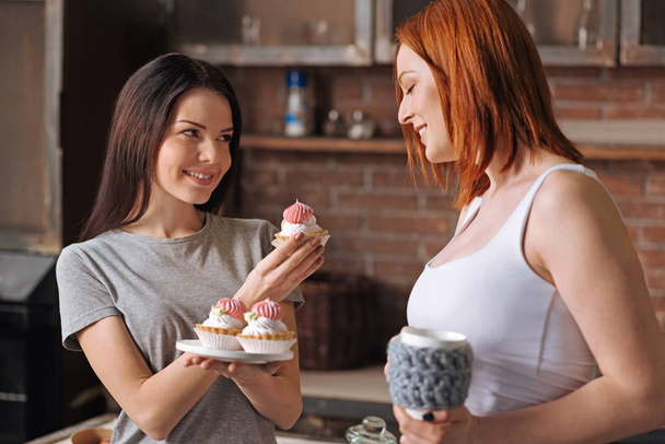 Positive delighted young female couple eating cakes - Foto, imagen