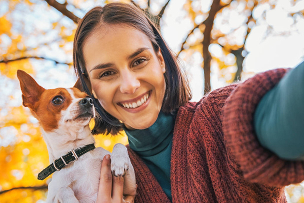 smiling young woman with dog outdoors in autumn making selfie - Foto, immagini