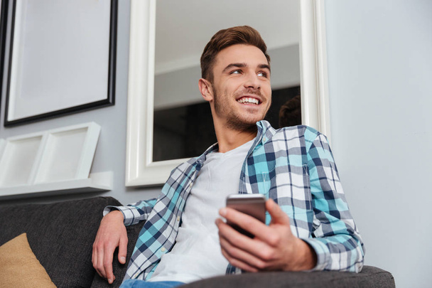 Happy man in home looking aside while chatting by phone - Foto, Imagem