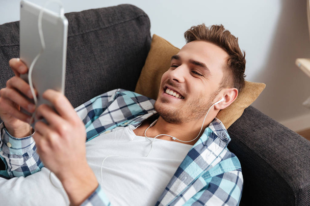 Vrolijke bristle man met behulp van de tablet pc tijdens het luisteren muziek - Foto, afbeelding