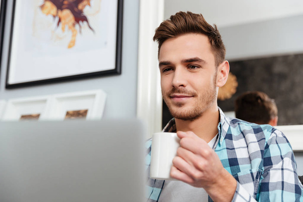 Happy young man using laptop computer while drinking coffee - Foto, imagen