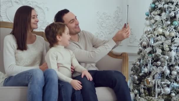 Happy young family of three taking selfies on sofa with tablet - Filmagem, Vídeo