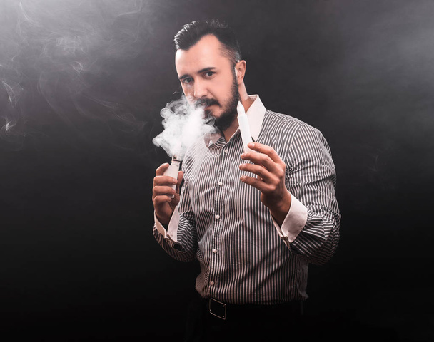 El hombre fuma cigarrillos electrónicos. Fumar y vapear en negro
 - Foto, imagen