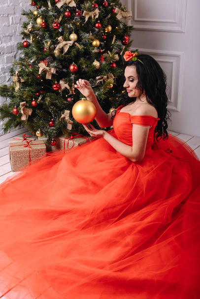 beautiful woman in the luxurious red dress decorates a Christmas - Φωτογραφία, εικόνα