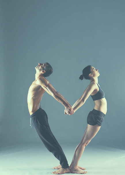 Young couple practicing acro yoga on mat in studio together - Фото, зображення
