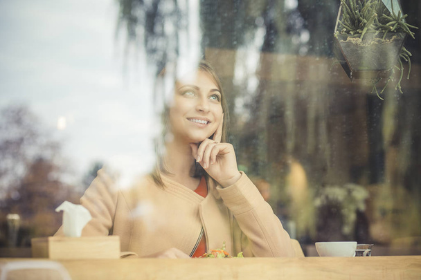 Beautiful young woman with coffee cup looking away at coffee shop - Foto, immagini