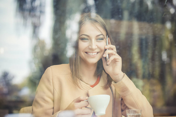 Businesswoman drinking coffee / tea and using phone computer in a coffee shop - Foto, immagini