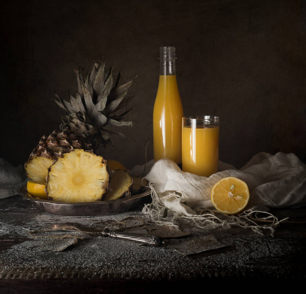 still life. pineapple, lemon, tropical juice, old silver knife on a wooden table - Фото, изображение