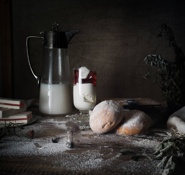still life, vintage. a simple country breakfast. milk, dessert, white bread, flour on  wooden table. dark background. - Photo, Image