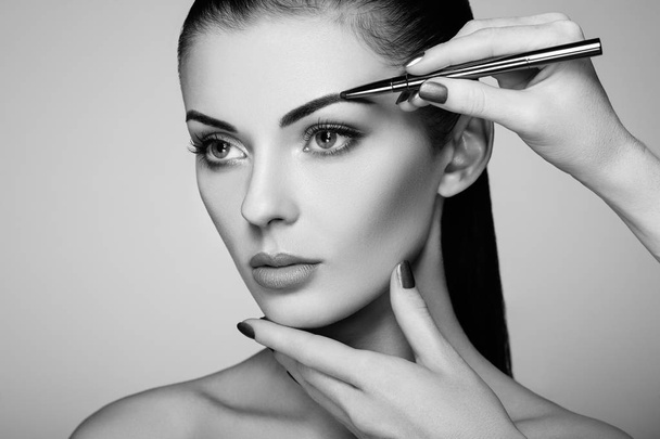 Beautiful brunette woman paints the eyebrows - Valokuva, kuva