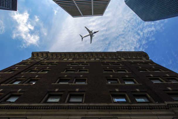 Низкий угол обзора Манхэттенских небоскребов с самолетом между ними
 - Фото, изображение