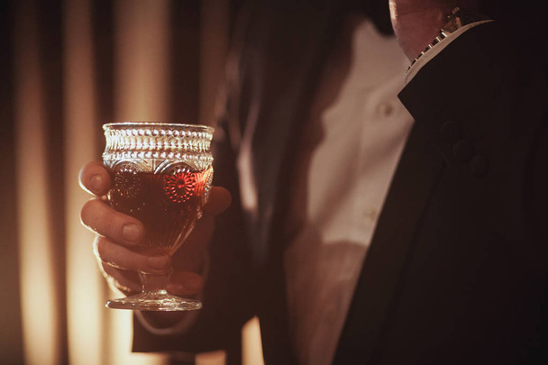 Mladý zázvor vousatý muž, který držel sklenici vintage s červeným vínem proti světlu, černá na pozadí - Fotografie, Obrázek