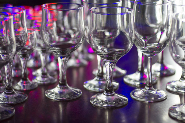 Lots of clean empty glasses of drinks on the bar in a nightclub. Glare and reflections on the glasses in the dark - Fotografie, Obrázek