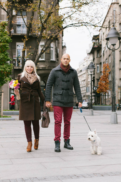 Счастливая пара гуляет с собакой на городской улице, смотрит в камеру
 - Фото, изображение