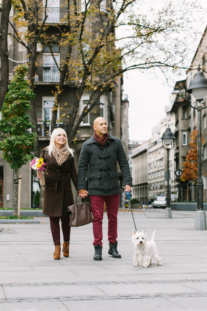 Happy couple walking with dog in city street - Photo, Image
