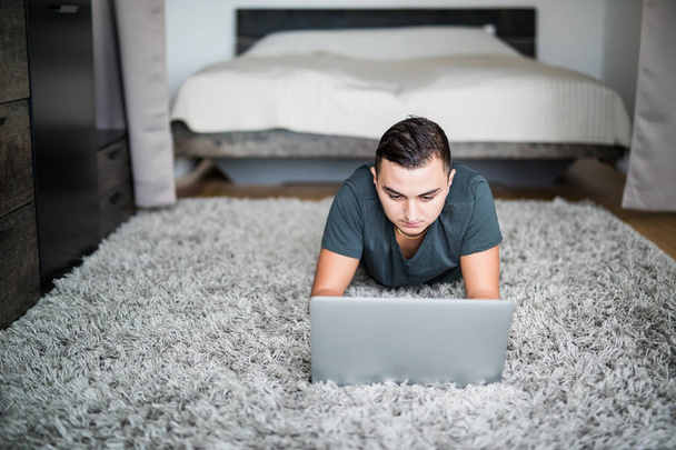 Jeune homme couché sur le tapis tout en utilisant un ordinateur portable
 - Photo, image