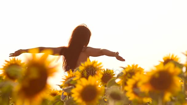 Szczęśliwa dziewczyna z włosami w lotach w wiatr, chodzenie w żółtych słoneczników, pole z złote kwiaty, słoneczny dzień lata. - Materiał filmowy, wideo