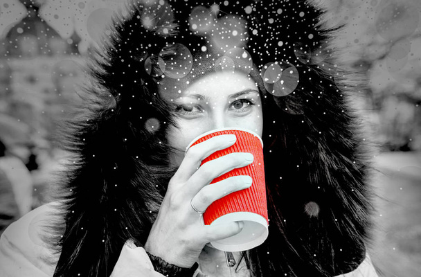 Yound girl drinks a red cup of hot tea black and white filtered with shiny snowfall with dramatic light - Photo, Image