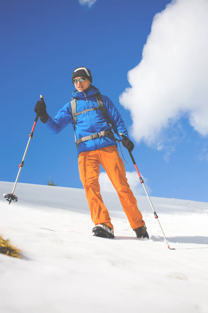 Mann mit Trekkingstöcken geht in den Bergen durch den Schnee. - Foto, Bild
