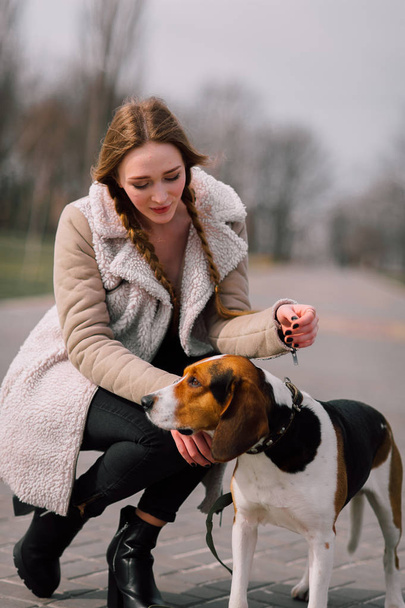 Young hipster girl with her pet estonian hound dog playing and having fun outdoor in the park. - Photo, Image