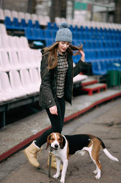 junges Hipstermädchen mit ihrem estnischen Hund, der im alten Stadion spielt, tobt und knutscht und Spaß hat. - Foto, Bild