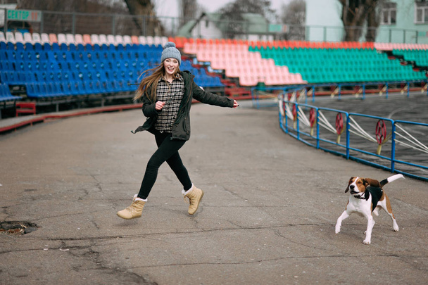 Jeune fille hipster avec son chien de chasse estonien animal de compagnie jouer, junping et câlins et avoir du plaisir en plein air à l'ancien stade
. - Photo, image
