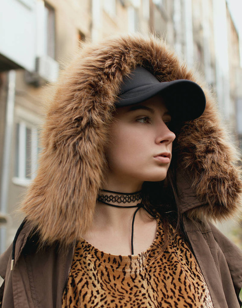 The girl in a cap and a leopard dress posing on the street - Фото, зображення