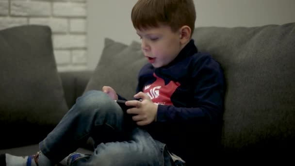 Young Boy Sitting on the Couch and Playing Games on the Smart Phone. - Кадри, відео
