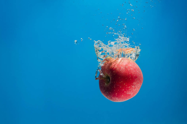Suda ıslatın ve bir sıçrama mavi zemin üzerine kırmızı elma - Fotoğraf, Görsel