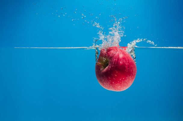Red apple in the water with a splash on  blue background - Foto, afbeelding